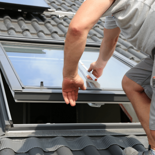 Man installing a roof window on a grey-slated roof