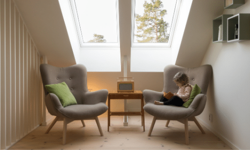 ttic space furnished with two grey love seats where a child is reading on one of the chairs and a side table
